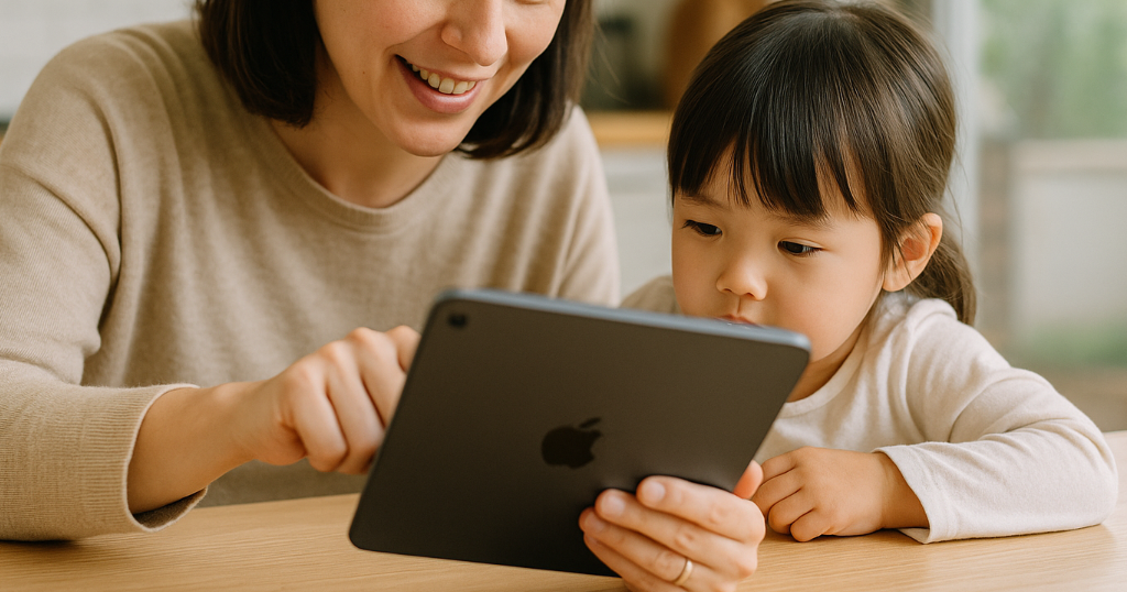 キッチンでiPadを見ながらレシピを確認する主婦と、隣で遊ぶ子ども。家事と育児の両立に役立つ様子